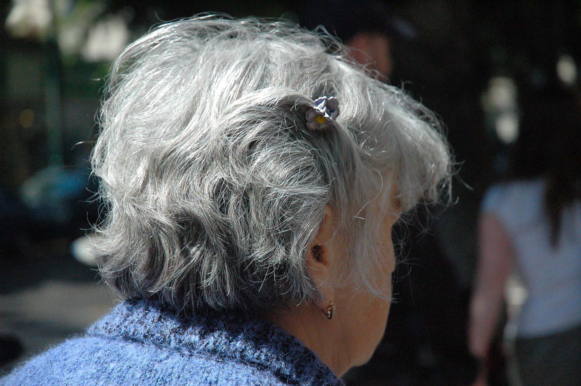 Older lady with short grey hair, with her back to the camera, wearing a blue cardigan